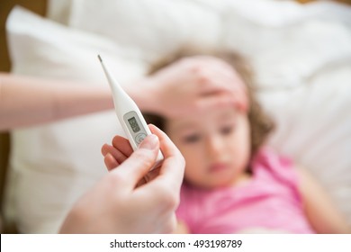 Close-up thermometer.  Mother measuring temperature of her ill kid. Sick child with high fever laying in bed and mother holding thermometer. Hand on forehead.  - Shutterstock ID 493198789
