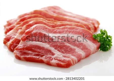 Close-up of thinly sliced raw pork belly, showing layers of meat and fat, with a sprig of fresh parsley on the side.