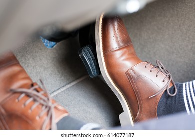 Closeup of a thirties man wearing brown shoes carrying a car accelerator and a brake / car safety system on the feet Accident and brake, danger of auto motor-driven bikes, driving habits