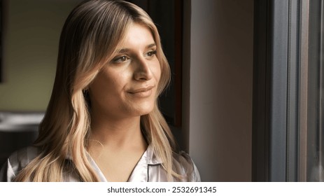 Closeup of thoughtful blond transgender woman looking through window at home - Powered by Shutterstock