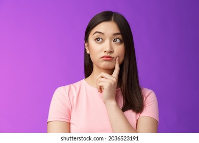 Close-up thoughtful cute asian girl dreamy standing purple background, touch cheek, turn left, thinking, doubting how act, wondering information, contemplating view from window - Powered by Shutterstock