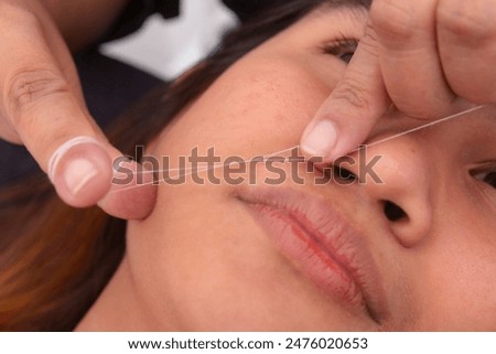 Close-up of threading technique being performed to remove unwanted upper lip mustache hair. Cotton thread used for precise hair removal.