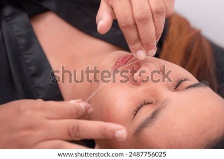 Close-up of threading technique being performed to remove unwanted upper lip mustache hair. Cotton thread used for precise hair removal.