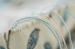 Closeup Of Threads Fraying From The Edge Of An Ivory, Blue And Brown Floral Pattern Fabric