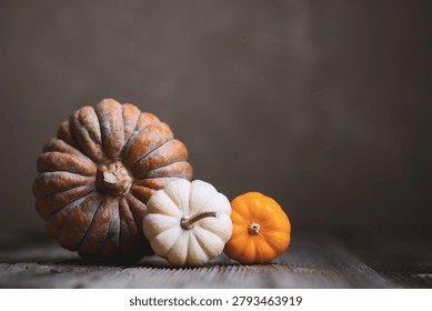 Close-up of three assorted pumpkins on wooden table against dark background in autumn setup. Moody food photography with seasonal styling and rustic fall atmosphere