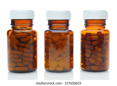 Closeup of three brown medicine bottles filled with different pills and medications with their caps on over a white background with reflection. Horizontal format.