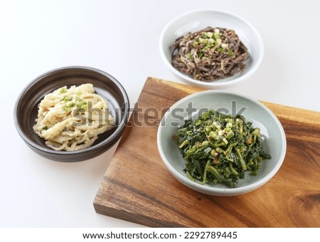 Close-up of three dishes with seasoned vegetables like spinach, balloon flower root and bracken on white floor and wood cutting board, South Korea
