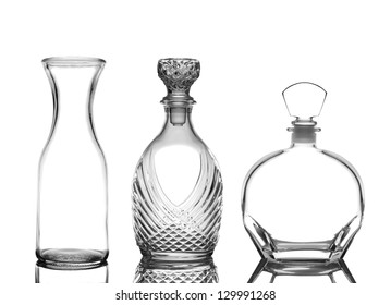 Closeup of three glass decanters on white with reflections. Wine Carafe and cognac decanters are depicted.
