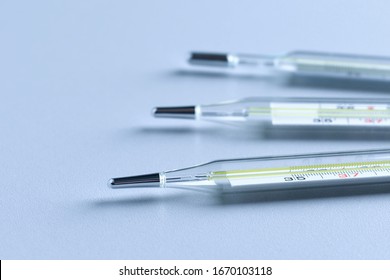 Closeup of three medical mercury thermometers on a gray table.