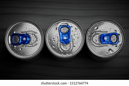 Close-up of three silver blue cans of popular energy drink top view, covered with water drops and isolated on dark background.