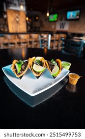 A close-up of three taco shells filled with beans and topped with lime wedges, served on a stylish plate in a dimly lit restaurant.