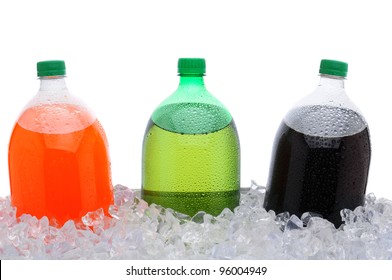 Closeup of three, two liter soda bottles in a large party style ice bucket. Only top half of bottles are visible. Lemon lime, orange and cola sodas over white.