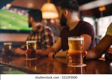 Closeup Of Three Young Men Sdrinking Beer In Bar And Watching Football Match