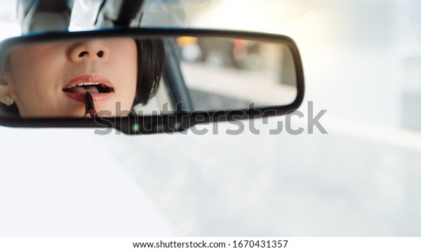 Closeup, Through rear mirror, face of stylish\
and beautiful middle aged Asian business woman executive put on\
makeup and lipstick in car in heavy traffic congestion during rush\
hour in city downtown.