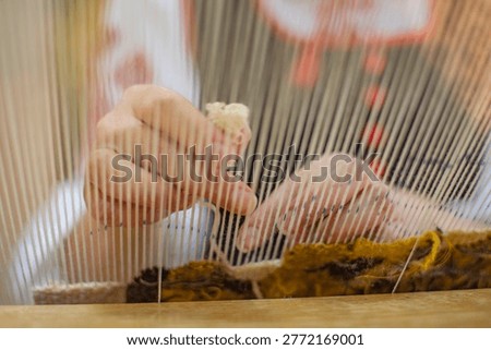 Close-up through warp threads of a weaver working at a manual loom. Authentic Belarusian textile craft, natural wool, soft lighting, creative process