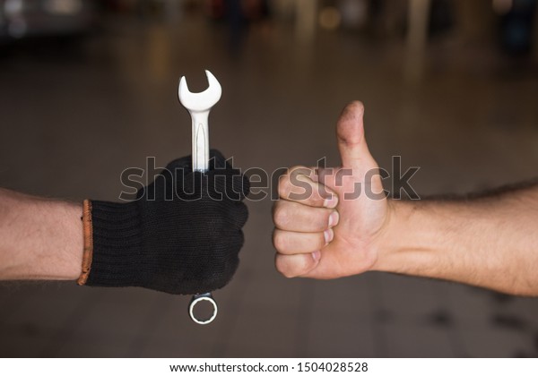 Close-up\
Thumb Up and Mechanics Hand with Tool. Automobile Master Wearing\
Gloves Showing Positive Gesture after Finishing Work. Technic\
occupation. Automobile Repair Service\
Concept.