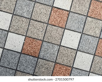 Close-up of a tiled surface with a grid of small square tiles in gray, beige, white, and terracotta tones. The alternating pattern creates a balanced geometric and textured design