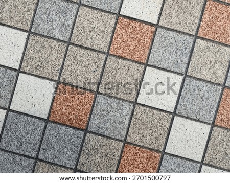 Close-up of a tiled surface with a grid of small square tiles in gray, beige, white, and terracotta tones. The alternating pattern creates a balanced geometric and textured design