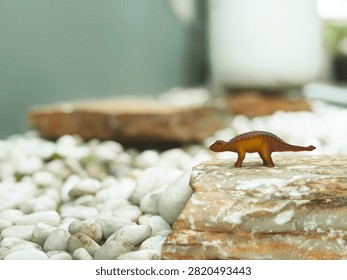 Close-up of a tiny dinosaur toy model on a large stone with shallow depth of field and soft lighting.