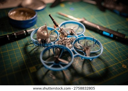 Close-up of a tiny FPV whoop drone during VTX repair on a cutting mat, showing exposed electronics, propellers, and a soldering probe in a detailed electronics workshop scene