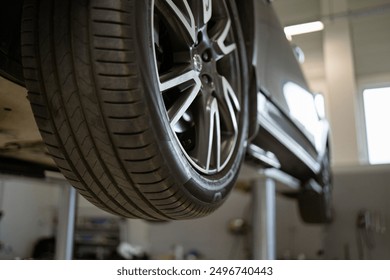 Close-up of tire on vehicle lift in auto repair shop showing car maintenance, inspection, tire check, and automotive detail. Industrial background with focus on tread pattern. - Powered by Shutterstock