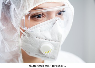 Closeup Of Tired Female Doctor,nurse Or Lab Tech Wearing PPE Protective Suit,white Face Mask And Goggles,lost Hope Due To Many Patient Deaths,looking At Distance With Sad Gaze,fear And Anxiety In Eyes