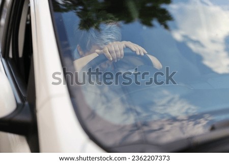 A close-up of a tired woman's hand on the car window during a daytime journey in the city.