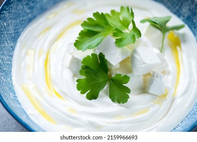 Closeup of tirokafteri or greek feta dip sauce topped with fresh parsley, olive oil and chunks of feta cheese, selective focus