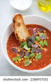 Close-up Of Tomato And Chickpea Soup Served With Fresh Basil And Ciabatta In A White Bowl, Vertical Shot On A Light-grey Stone Surface