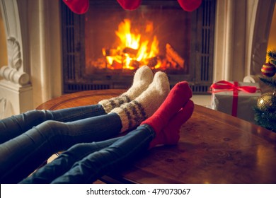 Closeup toned image of female and and feet in wool socks warming at fireplace at chalet