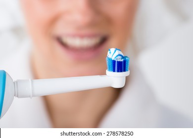 Close-up Of Toothbrush With Toothpaste In Front Of Woman