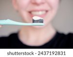 close-up of a toothbrush and toothpaste in a woman’s hands. woman in the background smiling and holding a toothbrush with toothpaste