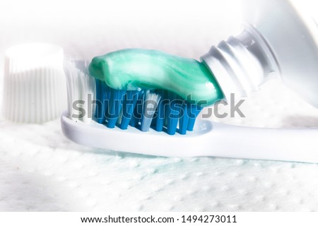 closeup of a toothpaste applied to a blue and turquoise toothbrush on a textured white background
