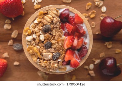 Close-up Top Down View Yogurt With Muesli, Strawberry, Cherry And Dried Raisins In A Brown Wooden Bowl On Wood Background.