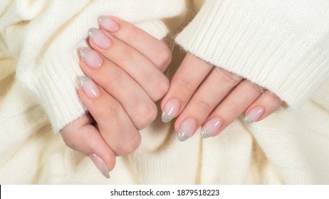 Closeup top view of beautiful natural look trendy manicure of  French nail design. Christmas pink nails with glossy silver isolated on white knitte background. Winter or autumn style of nail design.