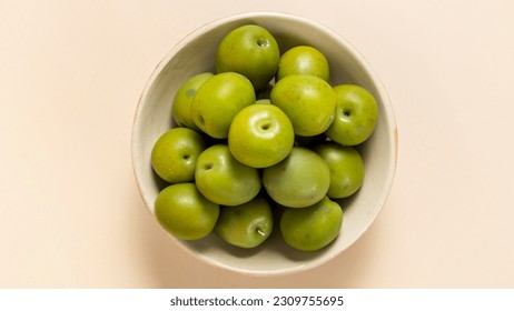 Closeup top view of bowl of delicious green olives with seed, against a soft neutral pale sandy color background. - Shutterstock ID 2309755695