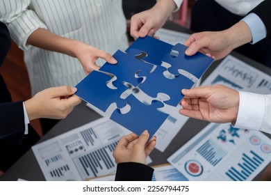 Closeup top view business team of office worker putting jigsaw puzzle together over table filled with financial report paper in workplace with manager to promote harmony concept in meeting room. - Shutterstock ID 2256794475