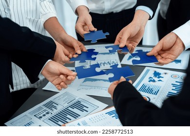 Closeup top view business team of office worker putting jigsaw puzzle together over table filled with financial report paper in workplace with manager to promote harmony concept in meeting room. - Shutterstock ID 2258772513