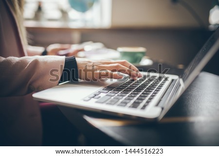 Close-up top view of Caucasian woman's hands Casually dressed student, blogger, writer man working on a laptop holding a phone in his hand, inside the cafe a wooden table and a cup of coffee.
