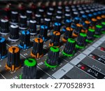 Close-up top view of colorful knobs on analog audio mixer with shallow depth of field. A macro photograph taken from above, focusing sharply on the tops of colorful control knobs (orange, green, blue) of an analog audio mixer. It highlights the "PAN" controls, with other channel strips receding into a soft bokeh background. Excellent for music production, studio tech, and audio engineering concepts.