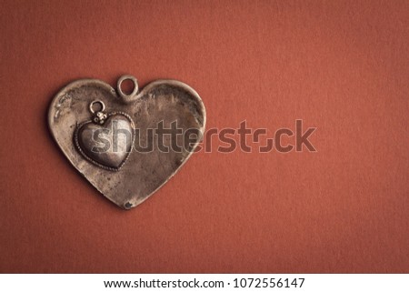 closeup top view detail concept of two small vintage metallic heart shaped jewels on top of each other on brown background with copyspace