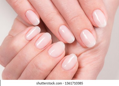 Nahaufnahme von eleganter pastellrosa Naturmanicure. Weibliche Hände einzeln auf weißem Hintergrund. Horizontale Farbfotografie.