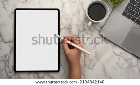 Close-up, top view of a female using stylus pen drawing on digital tablet touchpad computer on marble workspace.