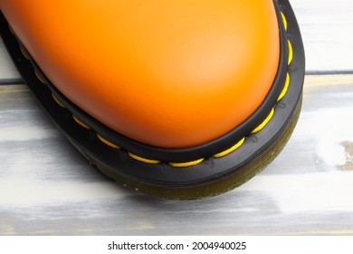 Closeup Top View On Bright Orange Color Tip Of One Single Leather Boot, Black Sole, Yellow Stitching On White Wood Background (focus On Toe Cap)