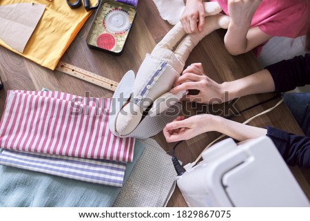 Close-up top view on the creative process of sewing rag bunny doll, details of doll cloth children hands sewing machine on the table background