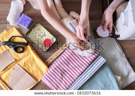 Close-up top view on the creative process of sewing rag bunny doll, details of doll cloth children hands sewing machine on the table background
