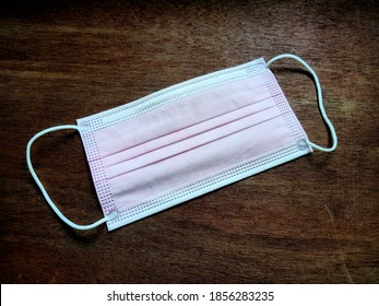 Close-up Top View Photo Of A Pink Disposable Mask Isolated On Wooden Ground. A Disposable Face Mask For Wearing To Protect Against Viruses And The Others When Out In Public, New Normal.