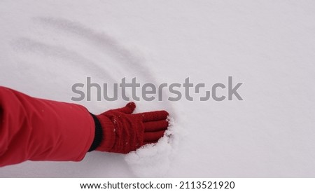 Closeup top view photography of female hand flattening fresh fluffy surface of white snow laying outdoor on snowy cold ground. Abstract natural background