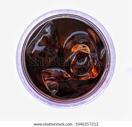 Closeup top view of a plastic glass of cola with ice on white background, selective focus.
