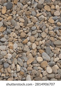 Close-up top view of smooth, rounded beach pebbles in various shades of brown, grey, and beige, creating a natural textured background